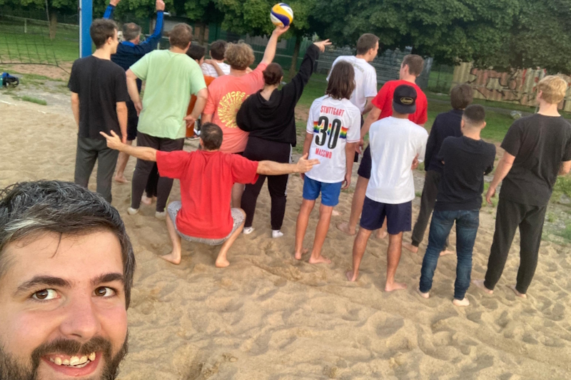 Gruppe von Jugendlichen steht am Rande eines Beach-Volleyball-Feldes mit dem Rücken zur Kamera.