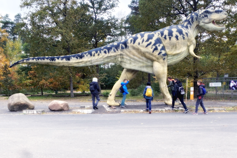 Eine Gruppe junger Menschen steht unter der Plastik eines Urzeit-Dinosauriers.
