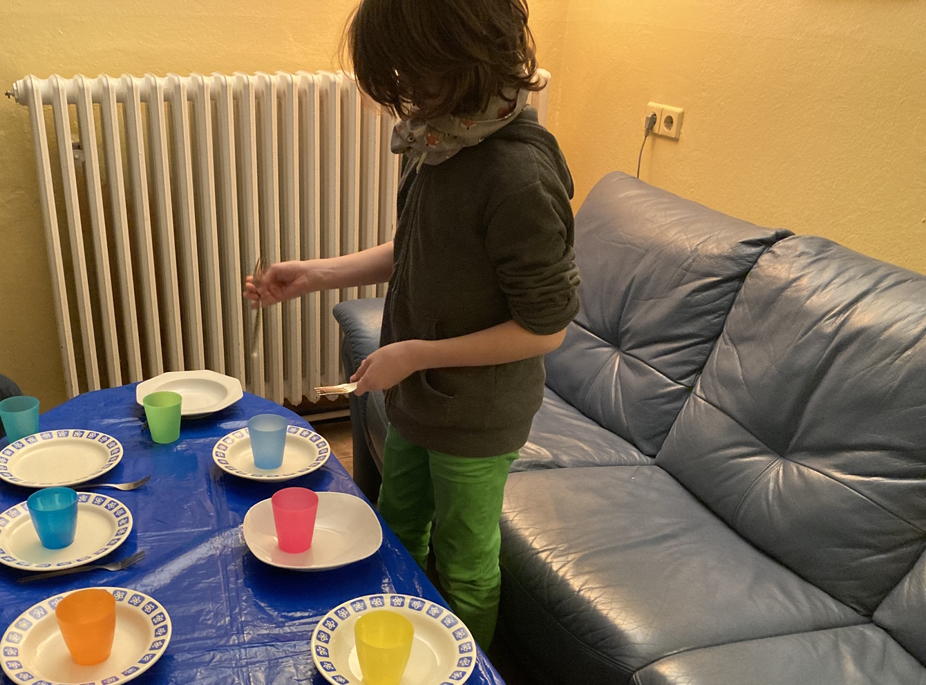 Ein Junge deckt den Tisch mit Tellern und bunten Bechern