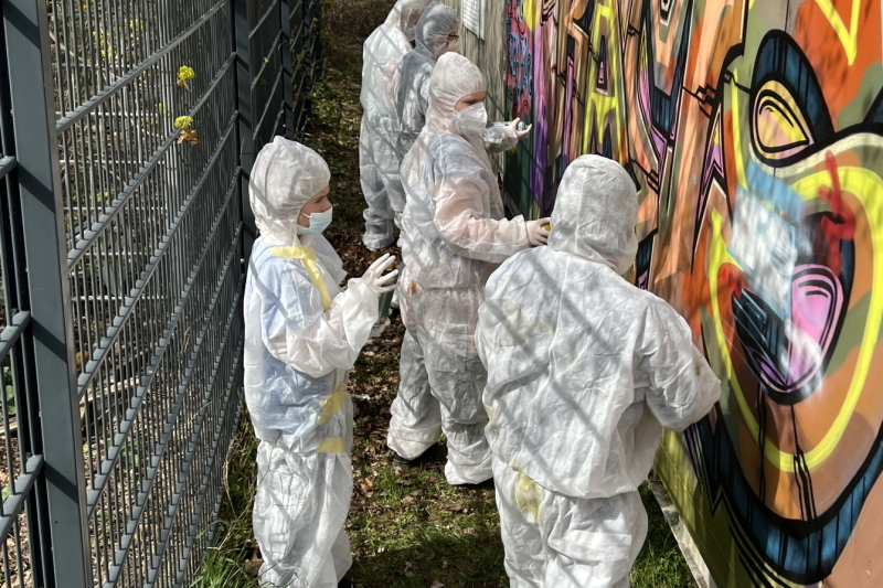Jungendliche in weißen Schutzanzügen vor einer Graffiti-Wand