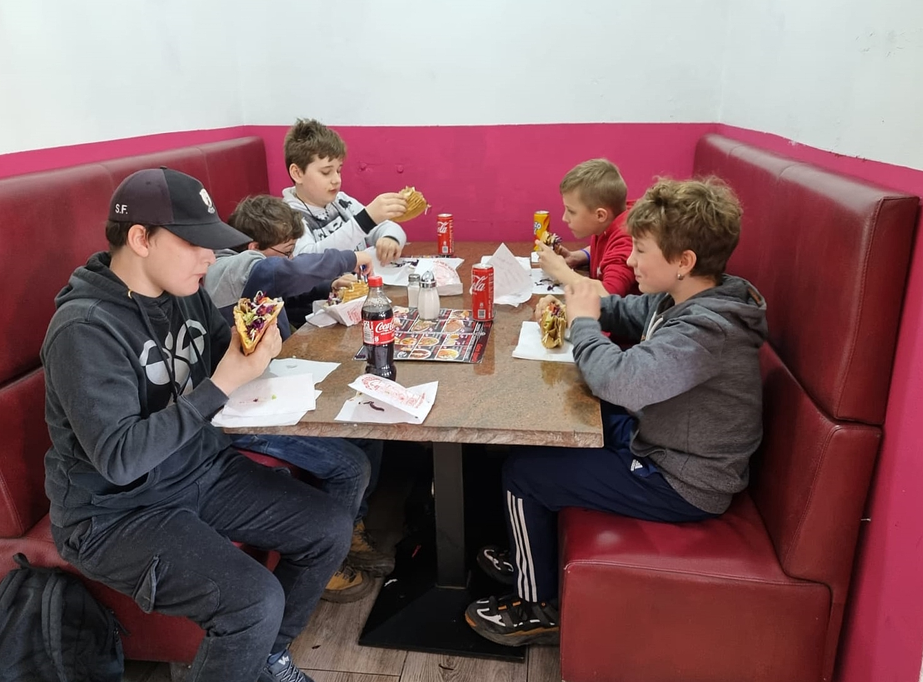 Vier Jungen sitzen an einem roten Tisch und essen Döner.