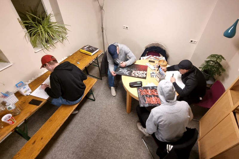 Vier Jugendliche sitzen an Tischen und zeichnen.