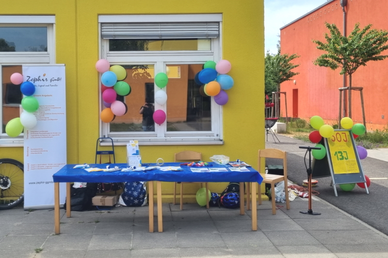 Tische mit Infomaterial, Luftballons vor dem gelben Haus der Grundschule am Buschgraben