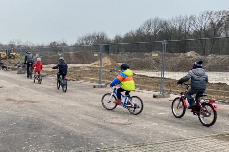 Kinder fahren mit ihren Fahrrädern in einer Reihe hintereinander auf einem Sportplatz